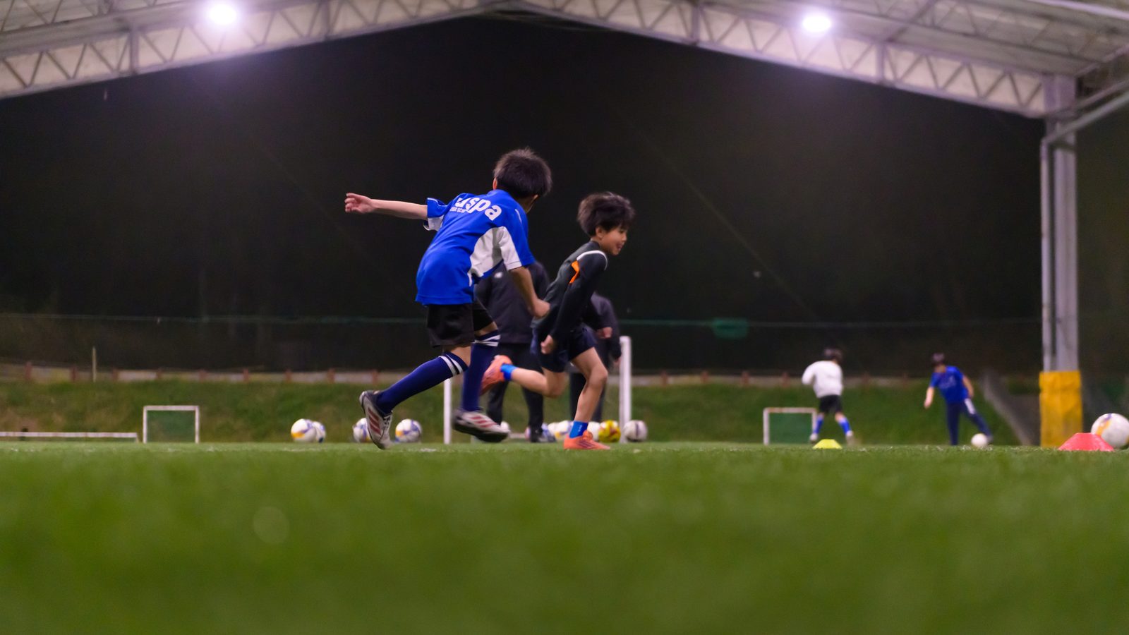 照明がついた夜のコートでドリブルする子どもたち